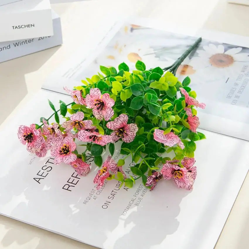 A bouquet of pink and green silk eucalyptus and violet artificial flowers displayed on a white paper.