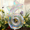 A large, iridescent, transparent number balloon shaped like the number 6 is displayed in a floral arrangement.