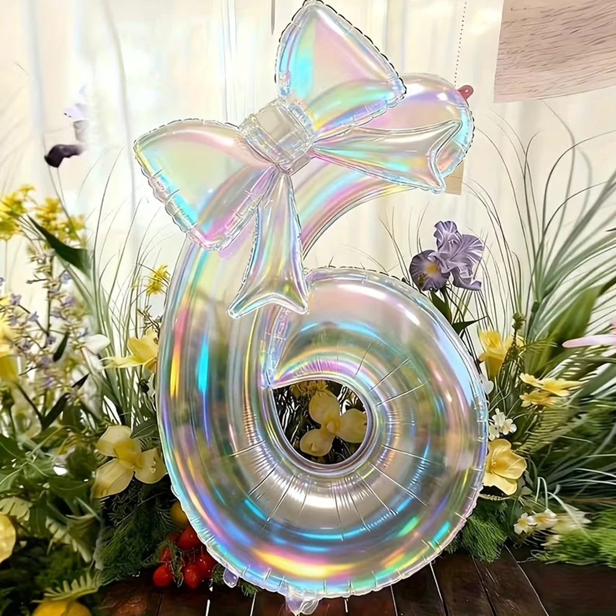 A large, iridescent, transparent number balloon shaped like the number 6 is displayed in a floral arrangement.