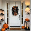 A black Halloween BOO wreath with an orange pumpkin garland hangs on a white door, decorated with spiders and candles.