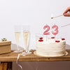 A white birthday cake decorated with pink candles shaped like the numbers 2 and 3 on a wooden table.