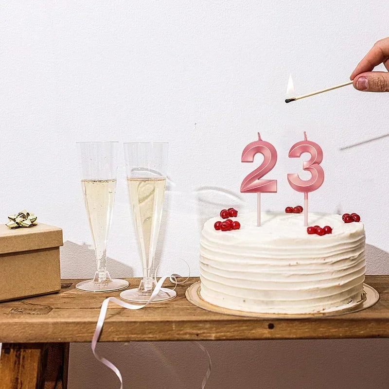 A white birthday cake decorated with pink candles shaped like the numbers 2 and 3 on a wooden table.