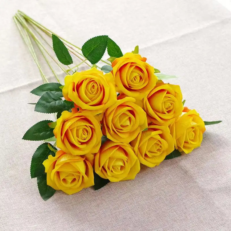 A bouquet of bright yellow velvet artificial roses with green leaves arranged on a light fabric.