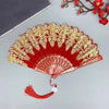 A red and gold elegant folding fan with traditional Chinese design displayed on a gray surface.