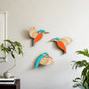 A set of three vintage wooden bird wall decorations in orange and blue hues mounted on a light gray wall.