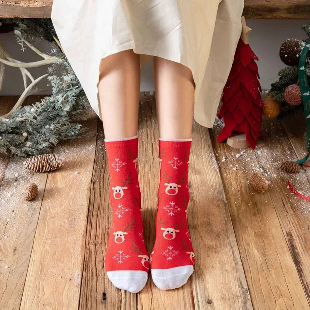 A pair of red Christmas socks featuring reindeer and tree patterns worn by a person in a white skirt.