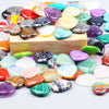 A collection of heart-shaped amethyst crystal stones in various colors and shades arranged on a wooden surface.