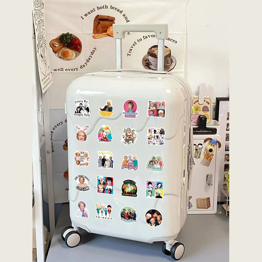 A white rolling suitcase decorated with various Golden Girls stickers and text