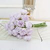 A bouquet of light purple silk peonies with green stems displayed on a white surface.