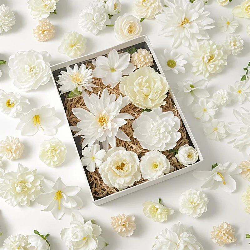 A collection of white and cream silk artificial flower heads arranged in a box with natural filler material.