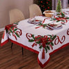 A white rectangle tablecloth decorated with red and green poinsettia patterns for a holiday table setting.