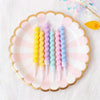 A plate holds several colorful spiral birthday cake candles with star toppers on a white fluffy surface.