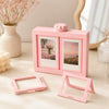 A pink 3D rotating photo frame is displayed on a light surface next to a vase of pink flowers.