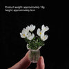 A hand holds a small glass vase filled with white tulips for home decor.