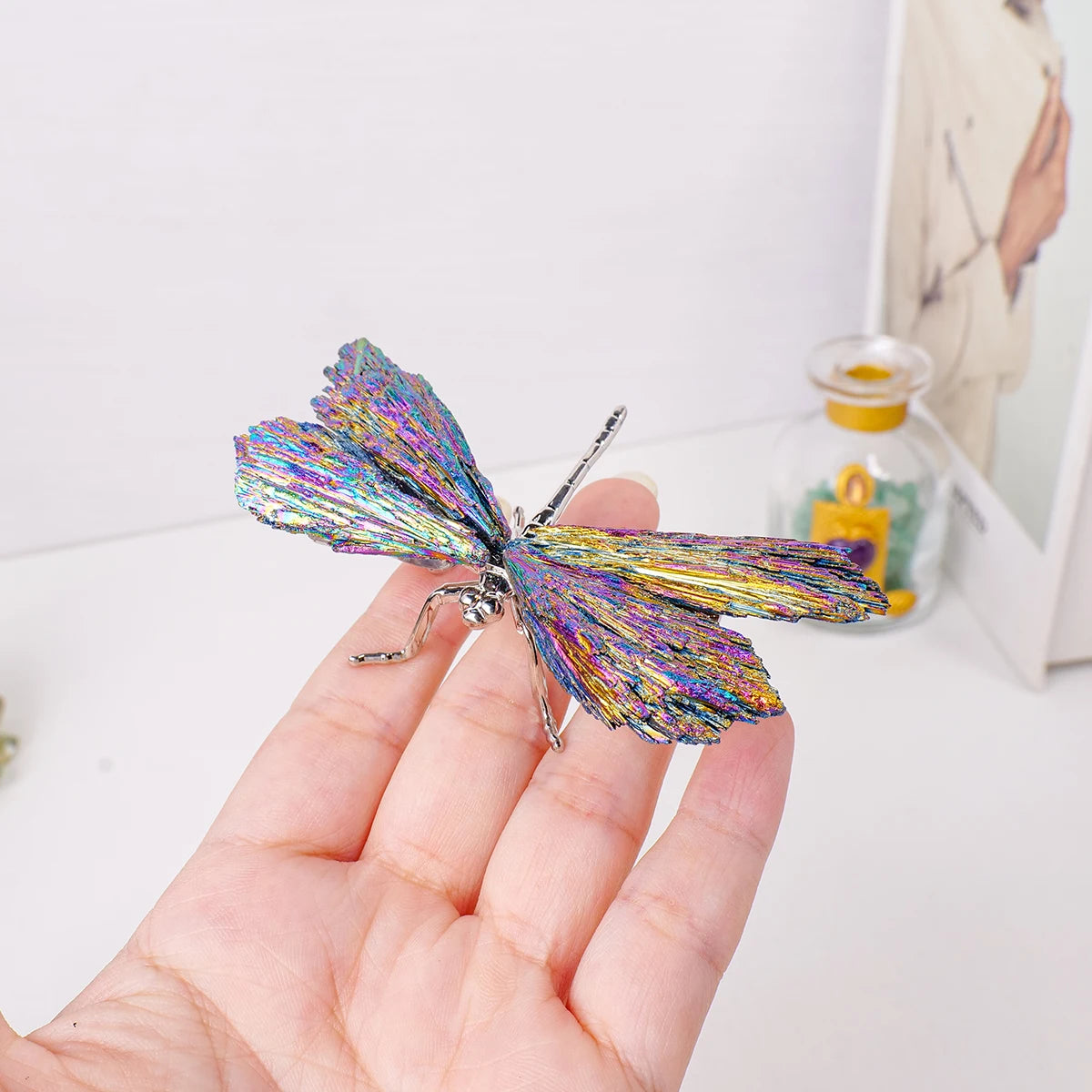 A hand holds a sparkling natural crystal tourmaline dragonfly figurine against a white background.