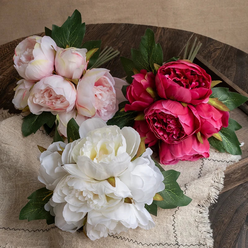 A bouquet of elegant artificial silk peonies in shades of pink and white resting on a beige linen cloth.
