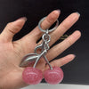 A silver charm featuring a pink glitter cherry pendant attached to a keychain, held by a hand.
