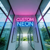 A bright neon sign spelling CUSTOM NEON is displayed in a modern glass hallway with vertical panels.