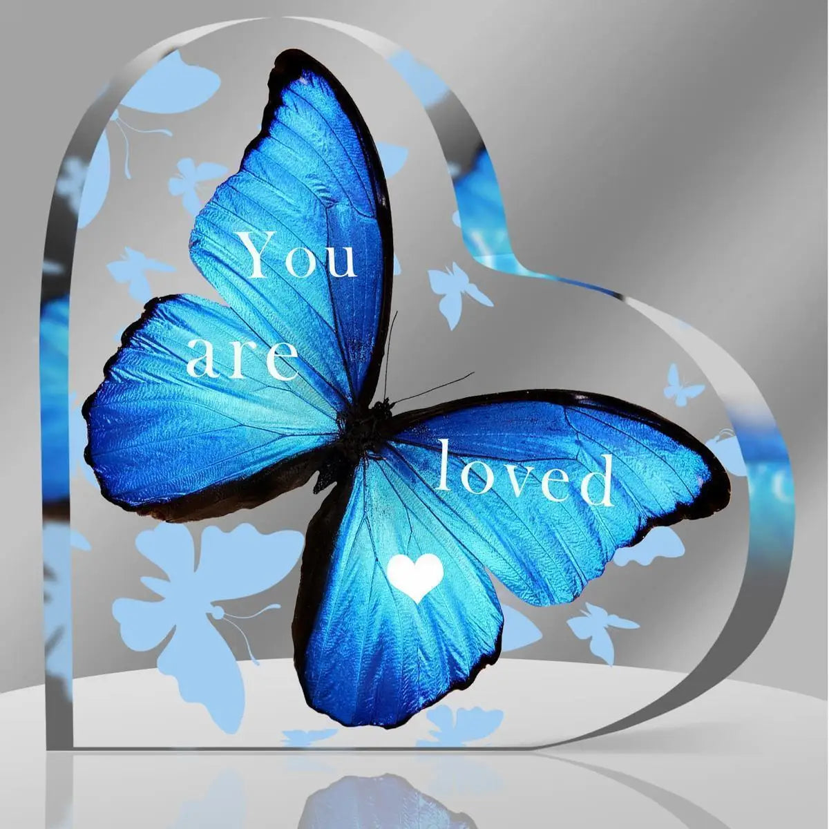 A vibrant blue butterfly with black wings is featured on a heart-shaped acrylic table decor, surrounded by inspirational text