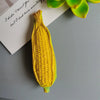 A bright yellow corn on the cob is placed next to a piece of paper with handwritten text and green leaves.