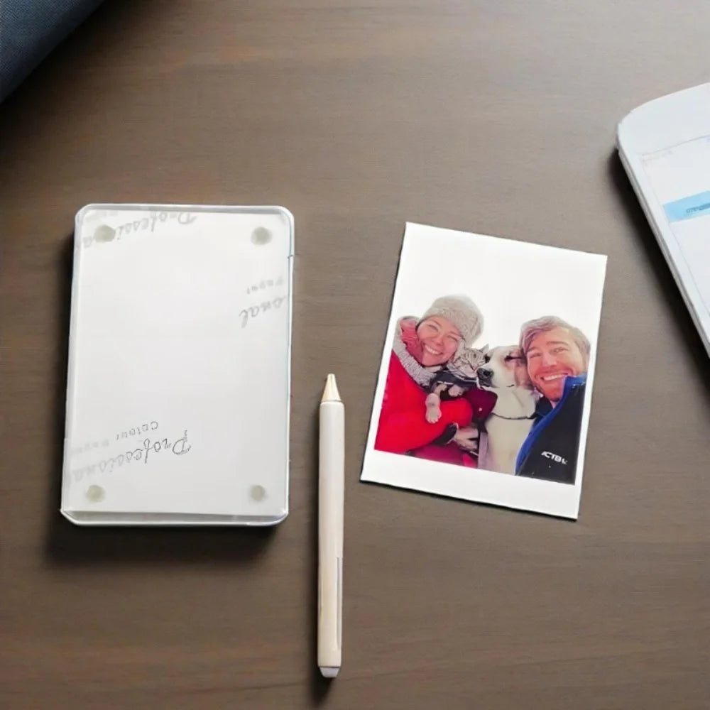A white photo frame with a magnetic visor clip holder and a pen are displayed on a dark wooden surface.