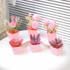 A set of six artificial potted plants in various shades of pink and purple displayed on a white surface.