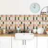 A kitchen countertop featuring a pink and green checkered tile backsplash, a white sink, and a round clock.