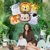 A woman sits with two young boys in front of a green foliage backdrop featuring foil balloons of safari animals like a lion, 