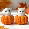 Three silicone molds shaped like a ghost, cat, and dog sit on an orange pumpkin against a white background.