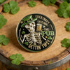 A commemorative coin featuring a skull and bones design with text that reads Everybody in the Pub Gettin' Tips