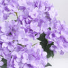 A close-up of a cluster of artificial purple hydrangea silk flowers on green leaves.
