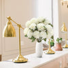 A vase of white artificial chrysanthemum flower balls displayed on a white countertop next to a gold-toned lamp.