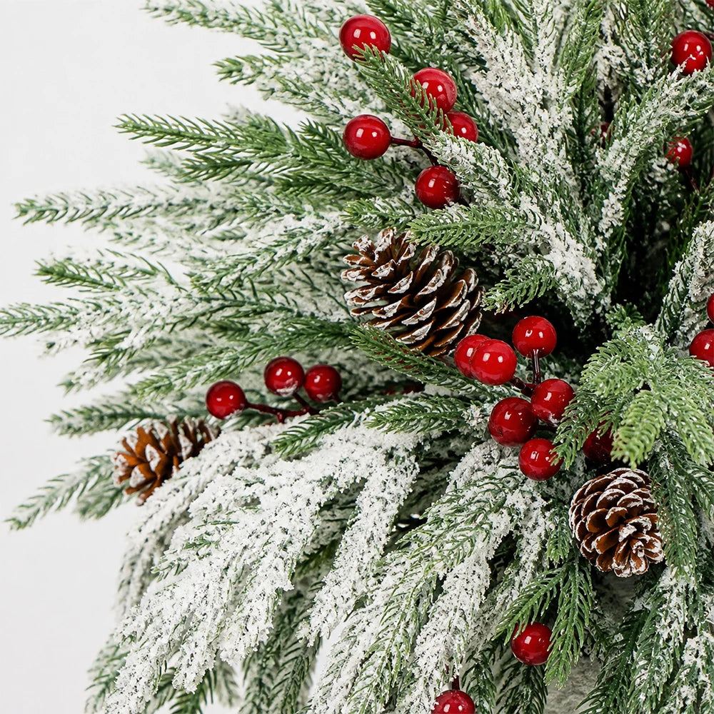 A festive wreath made of artificial evergreen branches covered in white flocking, decorated with red berries and pine cones.