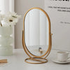 A gold-framed oval vanity mirror resting on a white surface next to a potted flower and a notebook.