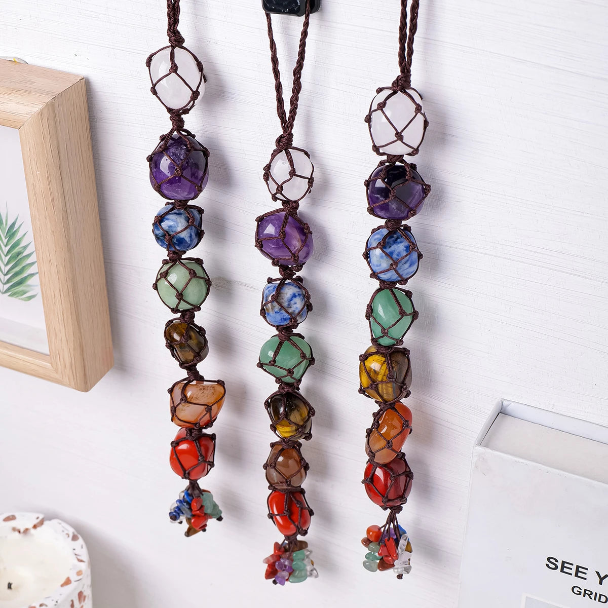 A set of natural crystal chakra rolling stone pendants hanging on a white wooden board.