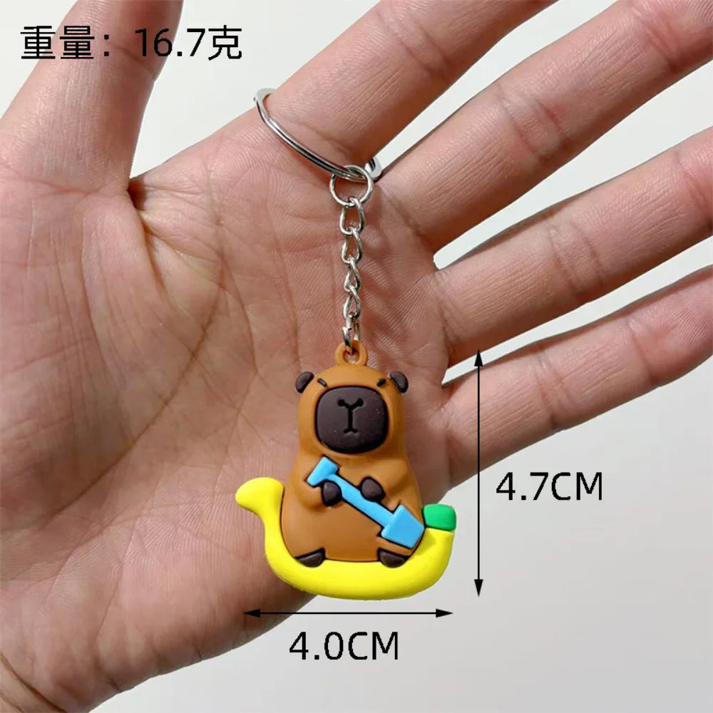 Clé-pendant de capybara brun rond avec un outil bleu, tenu dans une main.