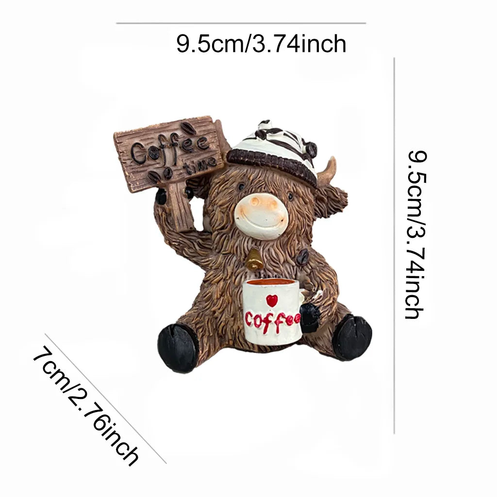 A brown cow figurine wearing a hat and holding a sign, with a cup of coffee visible.