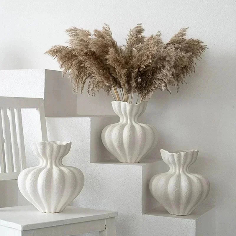 A grouping of white ceramic vases and dried grasses displayed on a white shelf.