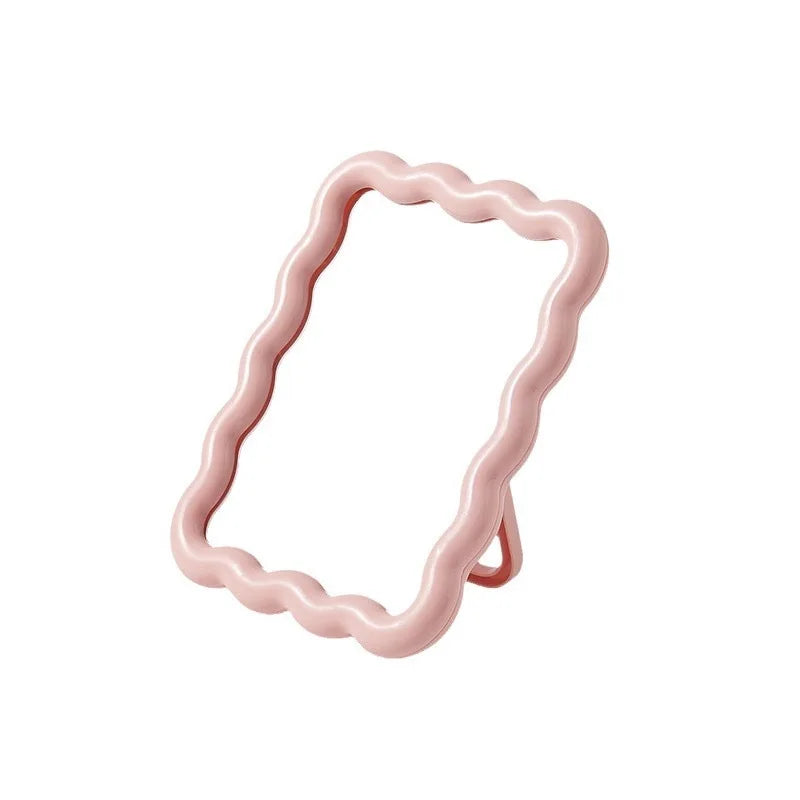A pink wavy frame makeup mirror with a stand.