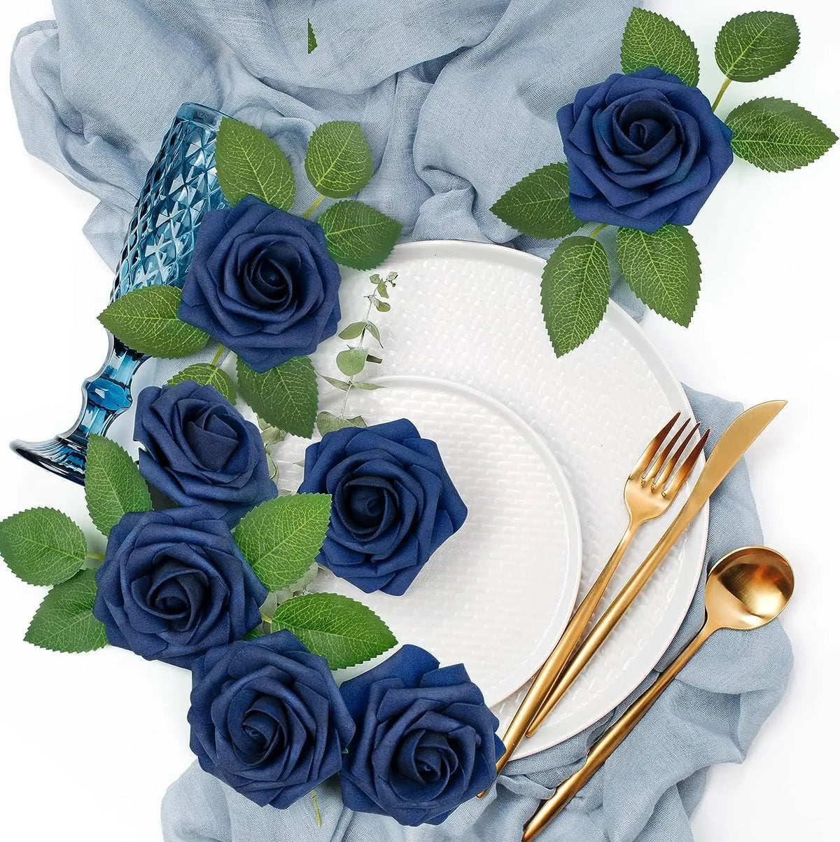 A bouquet of dark blue artificial foam roses and green leaves arranged on a white plate and light blue fabric.