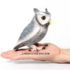 A realistic figurine of an owl perched on a human hand.