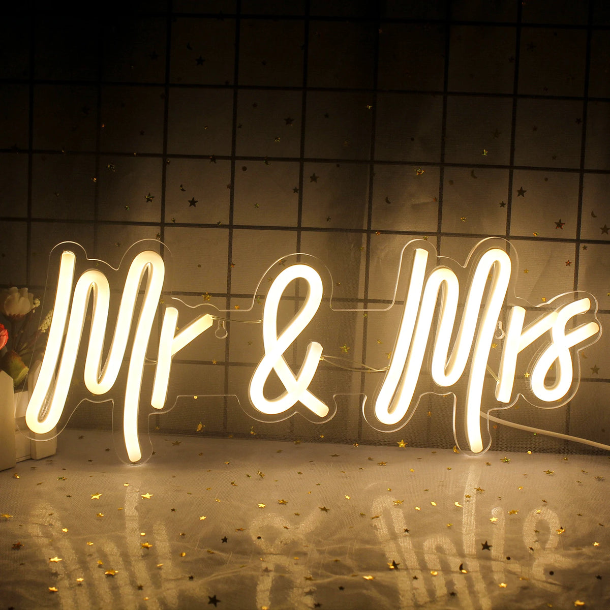 A neon sign spelling out Mr and Mrs with a sparkling gold confetti background.