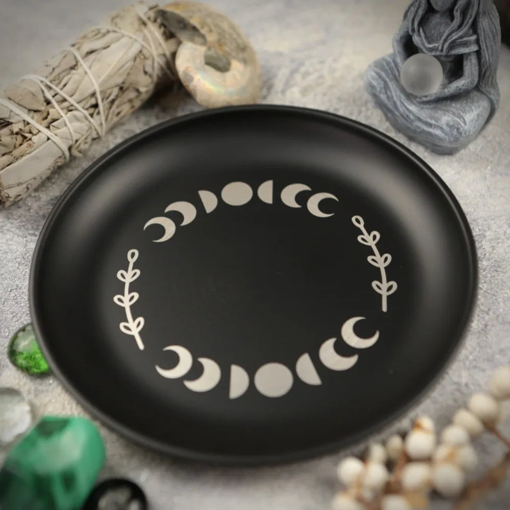 Assiette décorative noire avec un motif circulaire de symboles de croissant de lune et des accents de feuilles.
