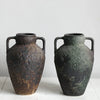 A pair of dark, textured ceramic vases with handles, showing a mottled brown and greenish-black glaze.