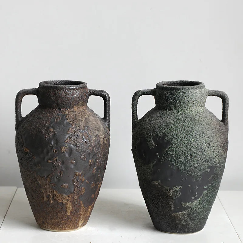 A pair of dark, textured ceramic vases with handles, showing a mottled brown and greenish-black glaze.