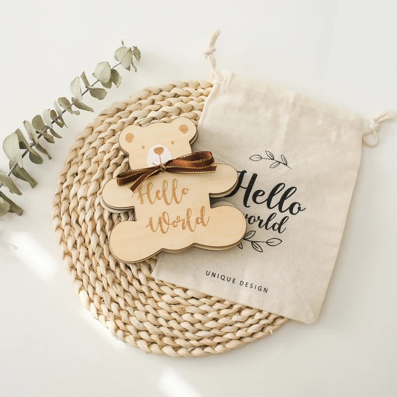 A set of wooden baby milestone cards featuring a bear design, resting on a woven mat and a linen pouch.