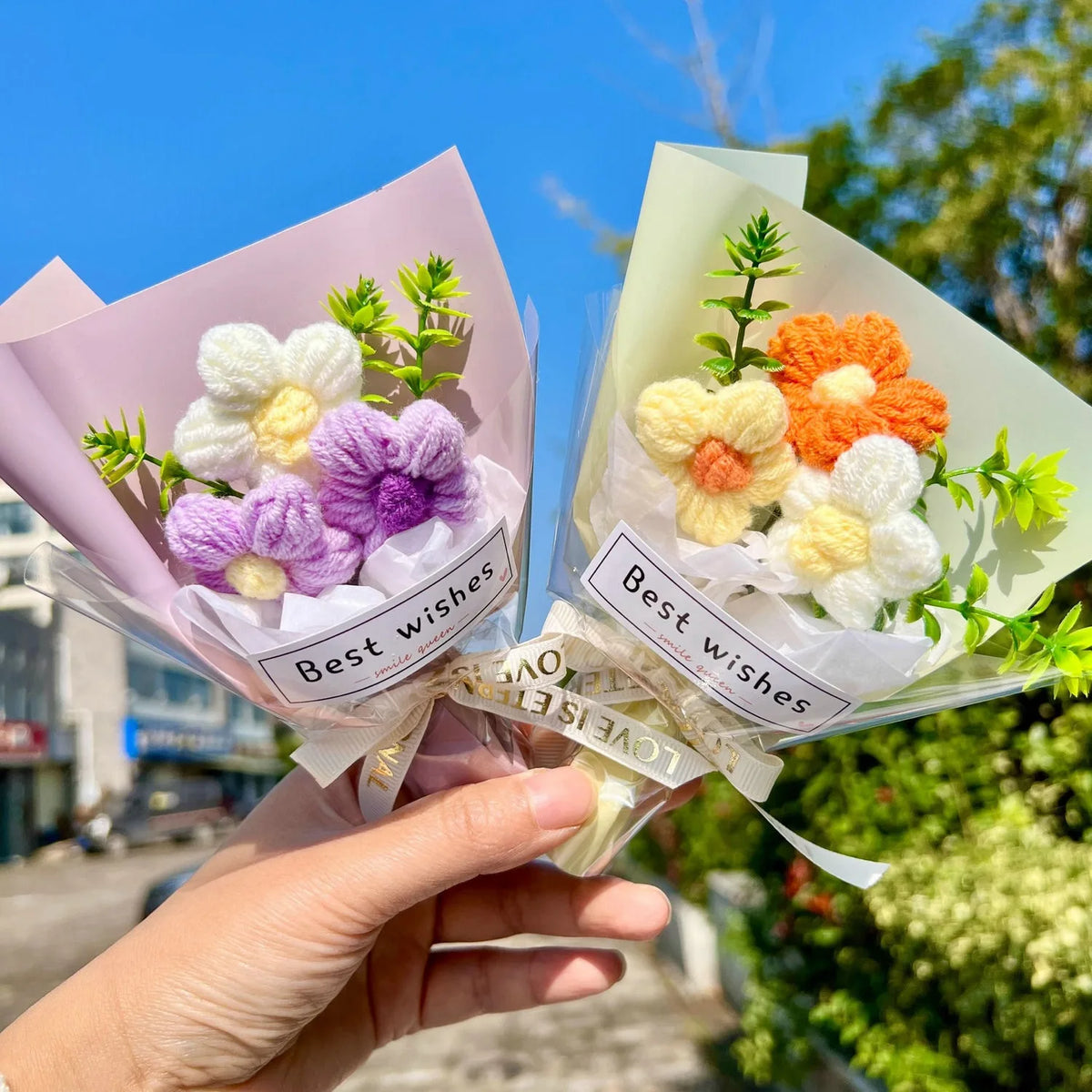 A hand holds a bouquet of handmade crochet flowers in pink and cream paper for special occasions.