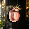 A pink suede cowboy hat with a floral arrangement is displayed on a dark door.