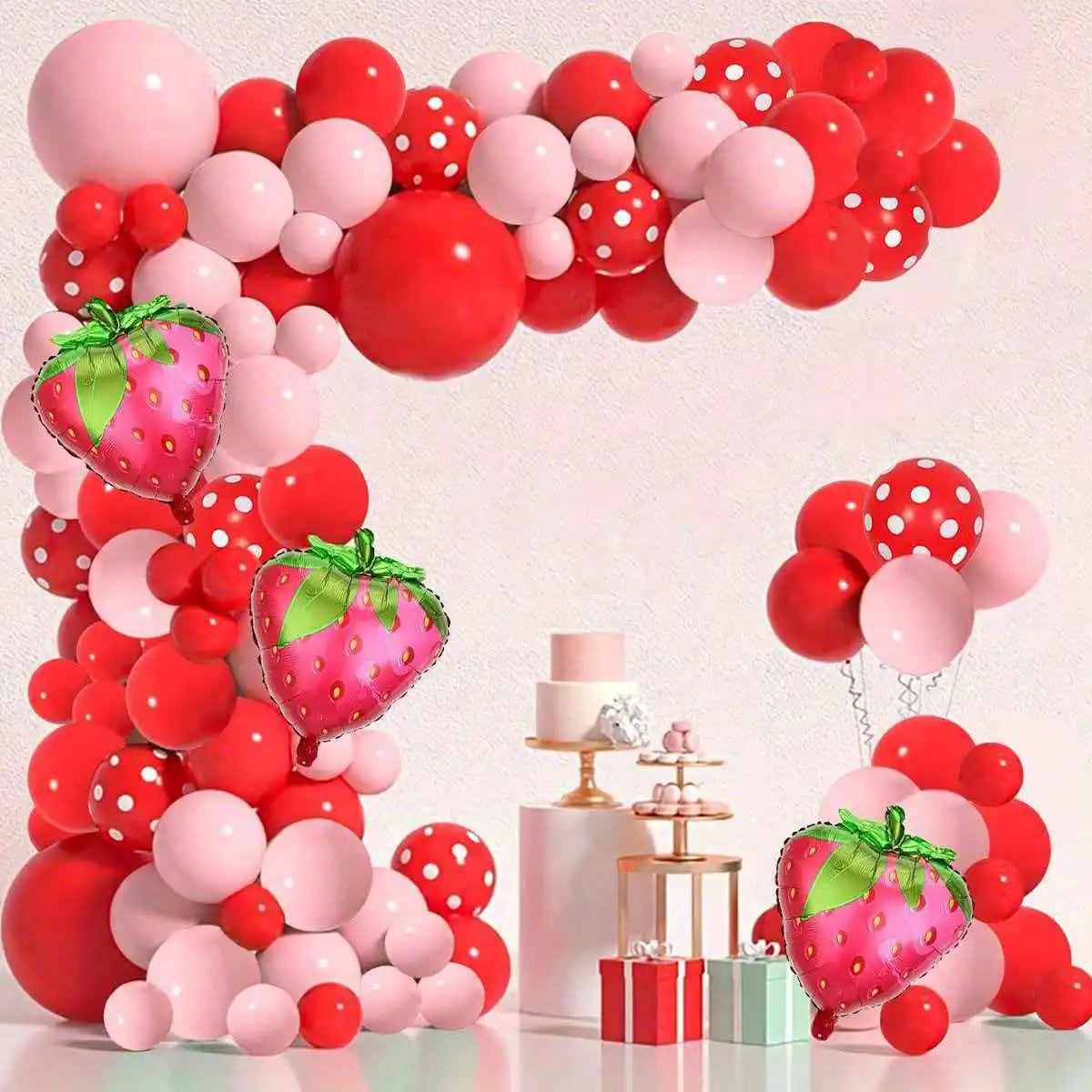 A vibrant balloon arch display featuring red and pink latex balloons shaped like strawberries.