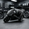 A dark figurine of a racing motorcycle rider in full gear is displayed on a desk with tools and tires in the background.